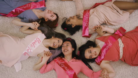 top view of bachelor girl and her friends holding hand lying on the carpet