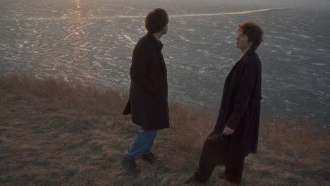 couple sharing cigarette and talking on frozen lake shore at sunset