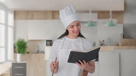 feliz mujer india chef profesional haciendo comida a partir de un libro de recetas