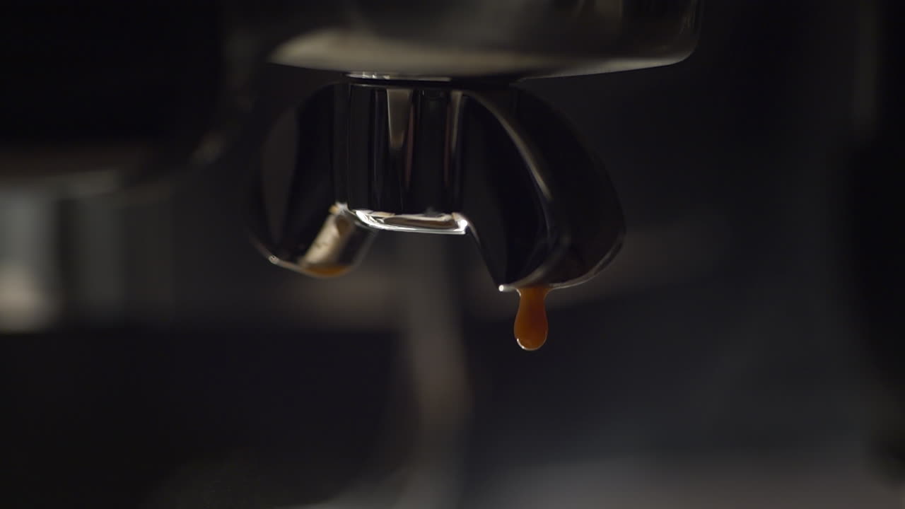 Macro in slow motion di caffè espresso che gocciola da un portafiltro lucido, evidenziando una crema ricca, un colore intenso e una texture raffinata. Illuminazione cinematografica e toni scuri creano un'immagine esclusiva per un prodotto di pregio.