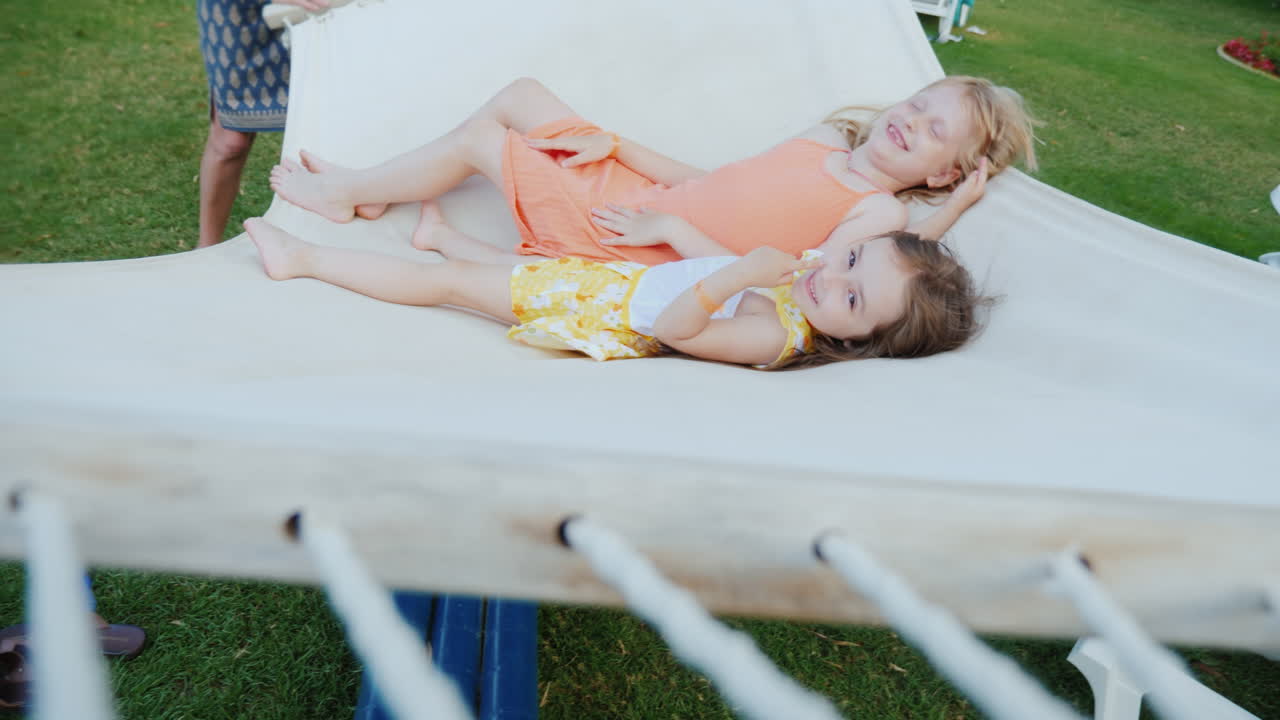 una joven madre sacude a sus hijos en una hamaca blanca divirtiéndose juntos riendo y disfrutando del