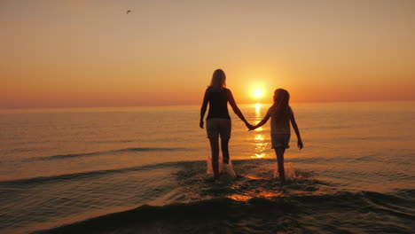 Mom-And-Daughter-Are-Walking-On-The-Water-Against-The-Backdrop-Of-The-Setting-Sun