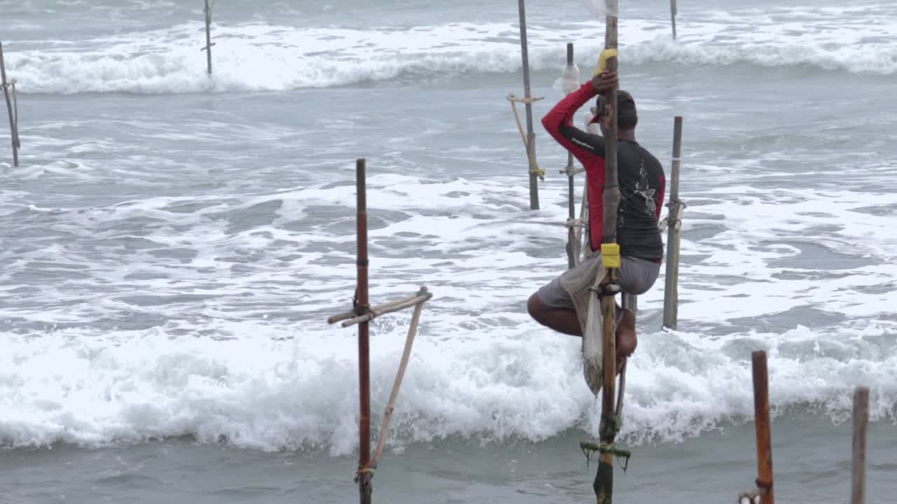 Isolated lonely Stilt Fisherman with a cap and bag ready for his job at the Weligama beach, empty stilts all around him