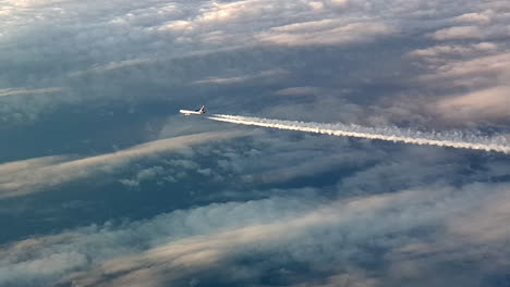 Vista-Increíble-Desde-La-Cabina-De-Un-Avión-Que-Vuela-Alto-Por-Encima-De-Las-Nubes-Dejando-Un-Largo-Rastro-De-Aire-De-Vapor-De-Condensación-Blanco-En-El-Cielo-Azul