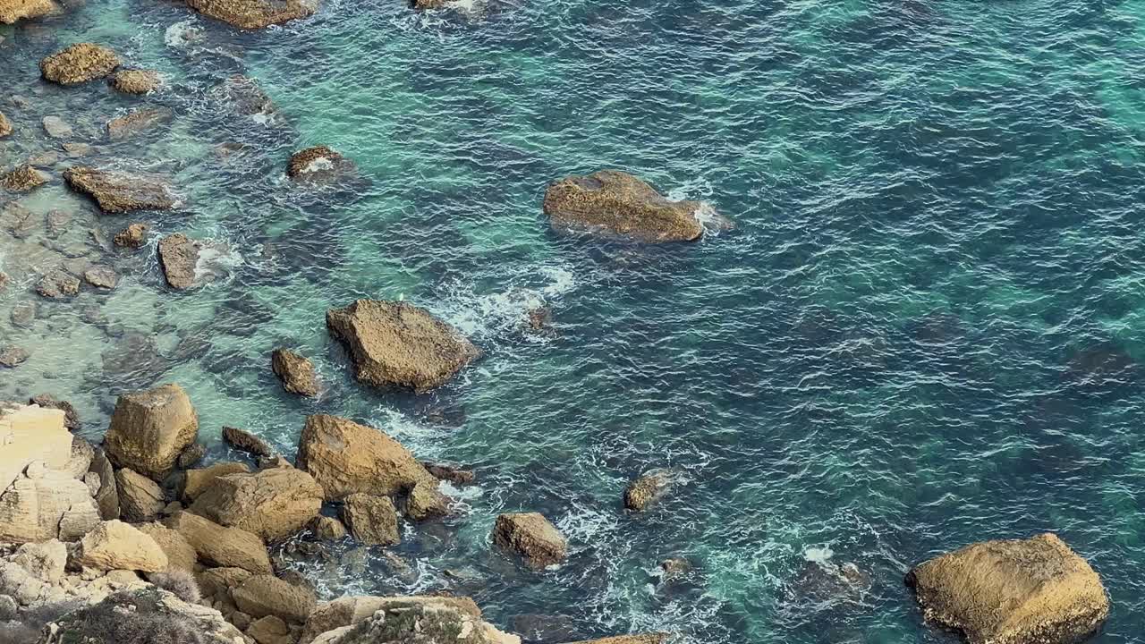 Acqua oceanica cristallina che si infrange dolcemente sulle rocce, vista da una scogliera