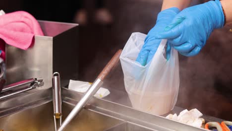 gloved hands pack soup into a plastic bag