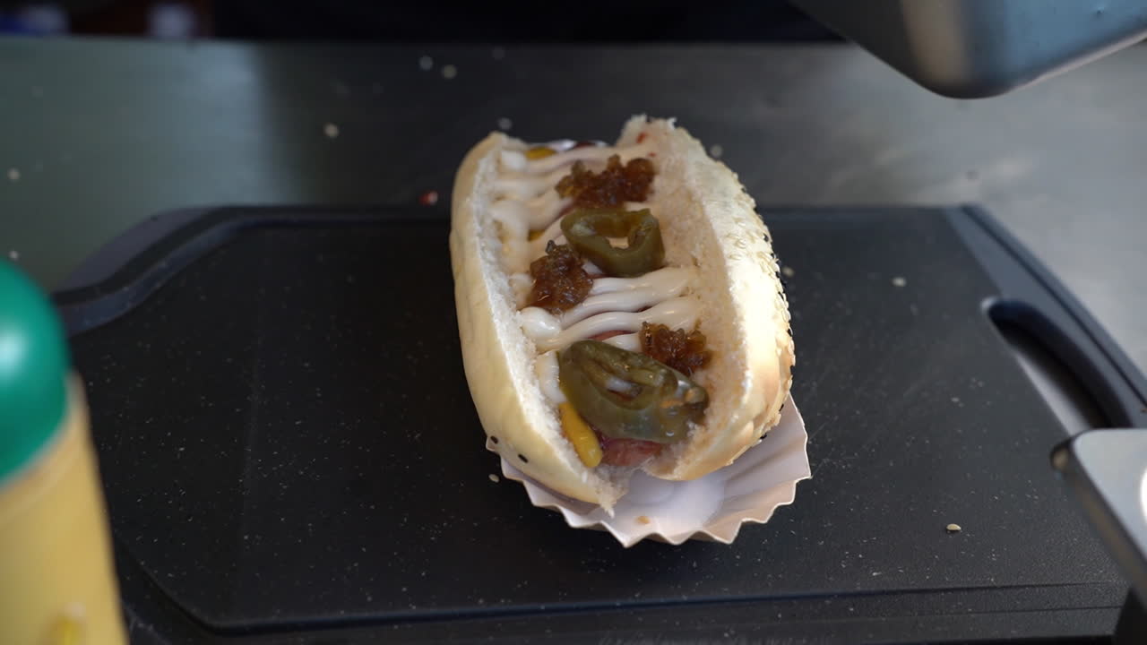 el equipo de servicio de alimentos agrega pepinillos encima del sándwich de perrito caliente con aderezo