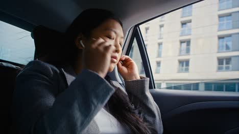 mujer china de negocios conduciendo en un taxi y usando auriculares