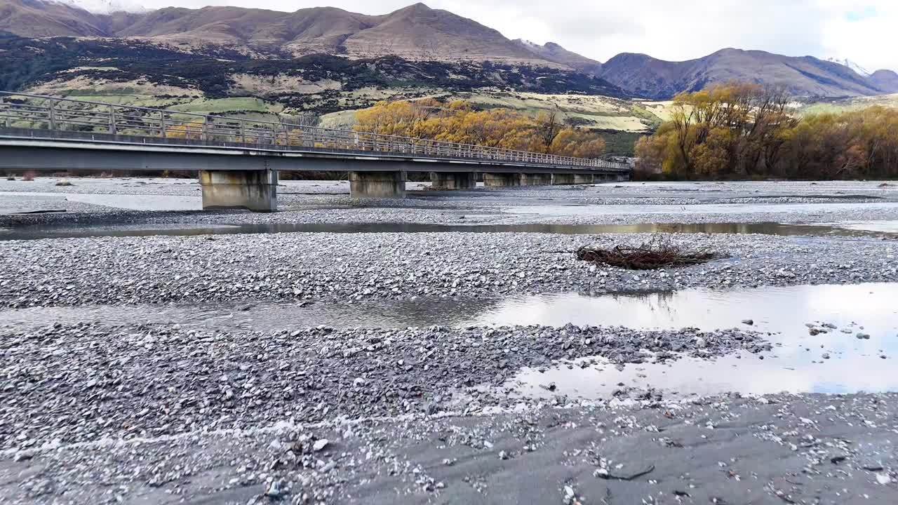 Aerial view of a bridge spanning a river with mountainous backdrop. Captured in natural light, highlighting autumn foliage and tranquil waters