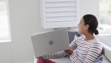 Glückliche-Biracial-Frau,-Die-Auf-Dem-Sofa-Sitzt-Und-Einen-Laptop-Für-Videoanrufe-Verwendet,-Zeitlupe