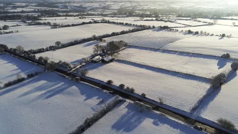 cold snowy winter british patchwork farmland countryside rural scene aerial slow orbiting left at sunrise