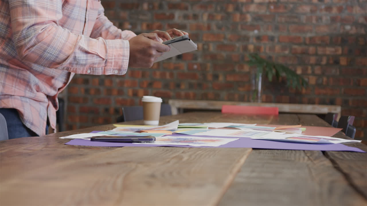 sección media de hombre afroamericano creativo usando tableta y mirando diseños, cámara lenta