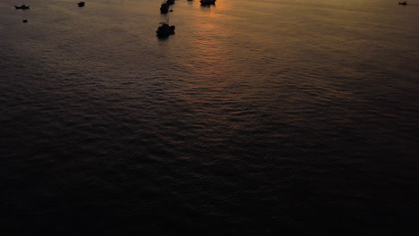 A-mesmerising-aerial-view-reveals-silhouettes-of-anchored-fishermen's-boats-seen-against-the-sun,-Mui-Ne,-VIetnam