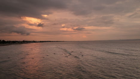 Crowd-of-surfers-paddle-and-wait-for-next-set-of-waves-at-sunset,-Canggu-Bali