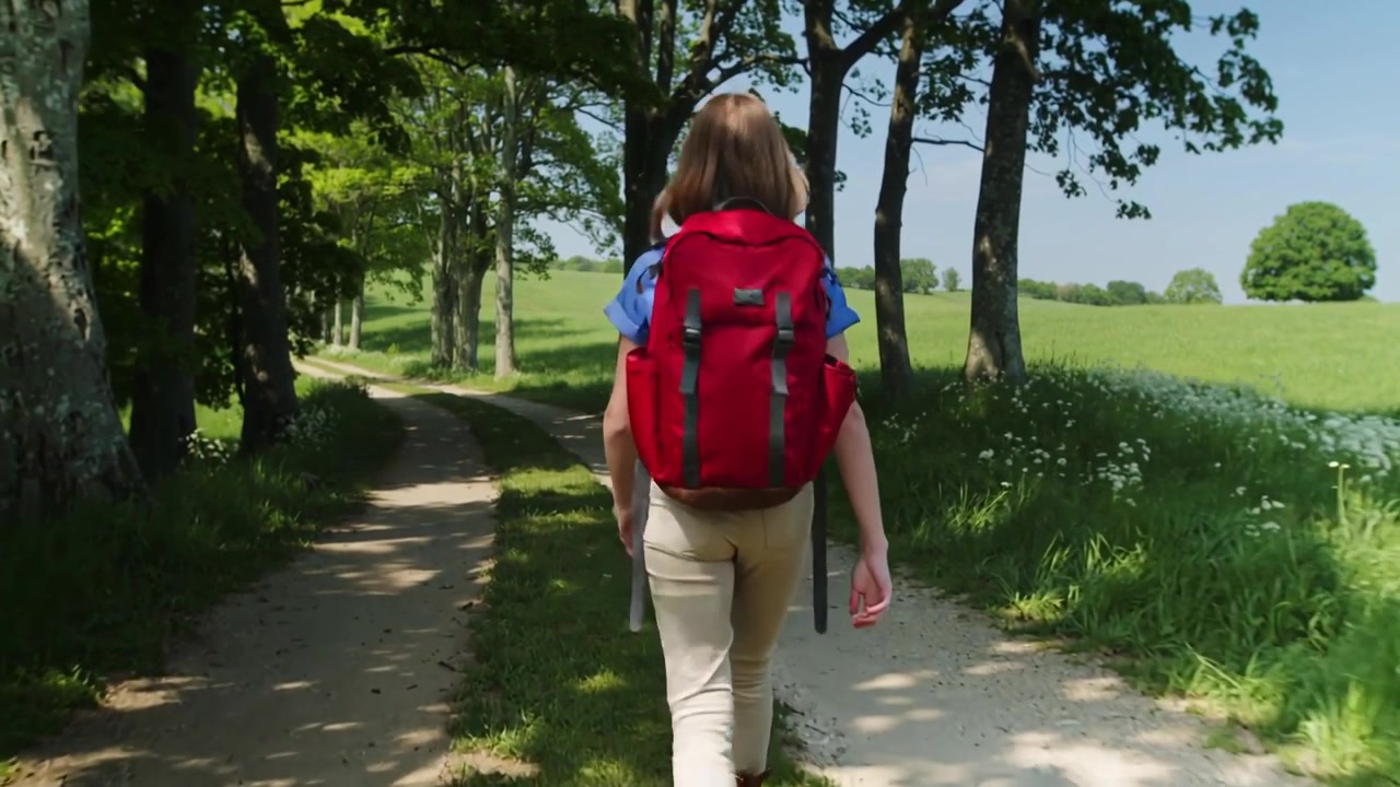 Starting, hiker walking tree-lined path with red pack, wearing blue-top beige-pants, toward meadow
