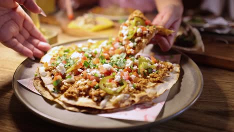 a hand lifts a slice of mexican tostada pizza from a plate in a warmly lit bangkok restaurant, with shallow depth of field and inviting ambiance