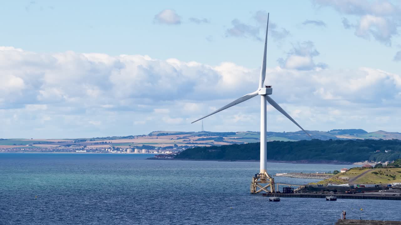 Large offshore wind turbine spins steadily in bright daylight over calm Dundee coastal waters