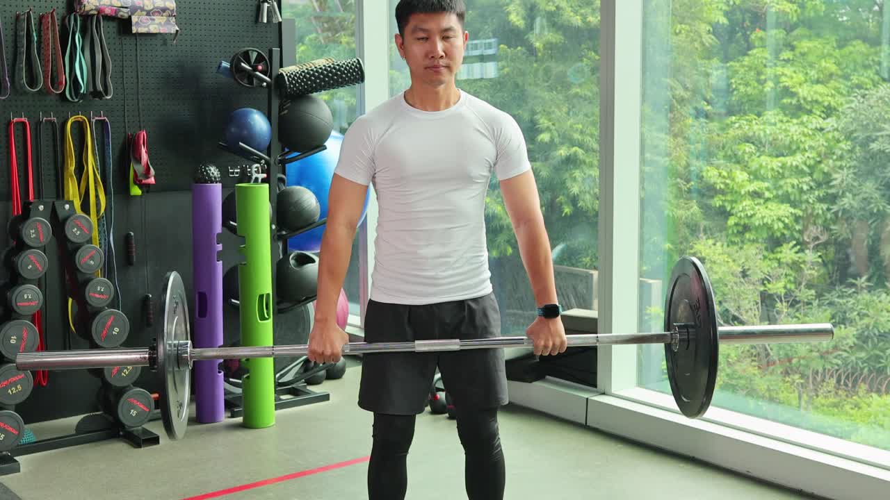 Athletic man performing barbell deadlift in bright, modern gym with natural daylight and equipment