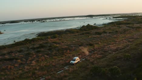 toma aérea dinámica de todoterreno con una carpa en la azotea que atraviesa un campo áspero y levanta polvo