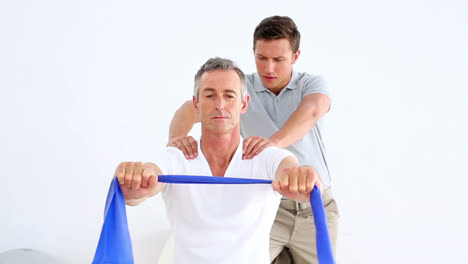 Physiotherapist-checking-patient-stretching-blue-resistance-band