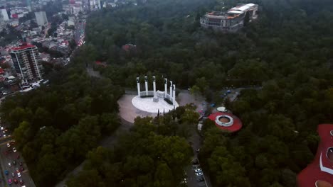 Tilt-down-aerial-orbit-of-the-Altar-a-la-Patria-in-Chapultepec-forest-in-Mexico-City,-winter-fog,-drone-shot