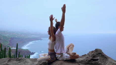 en la cima de una montaña, un hombre y una mujer se sientan de espaldas en una roca, encontrando consuelo a través de la meditación y el yoga contra el fondo del océano.