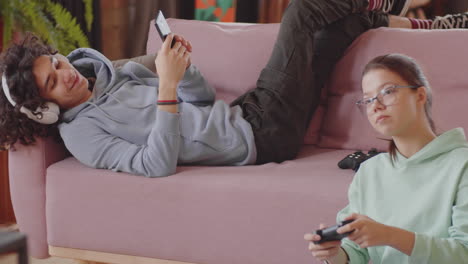 teenage kids playing console game and using smartphone at home