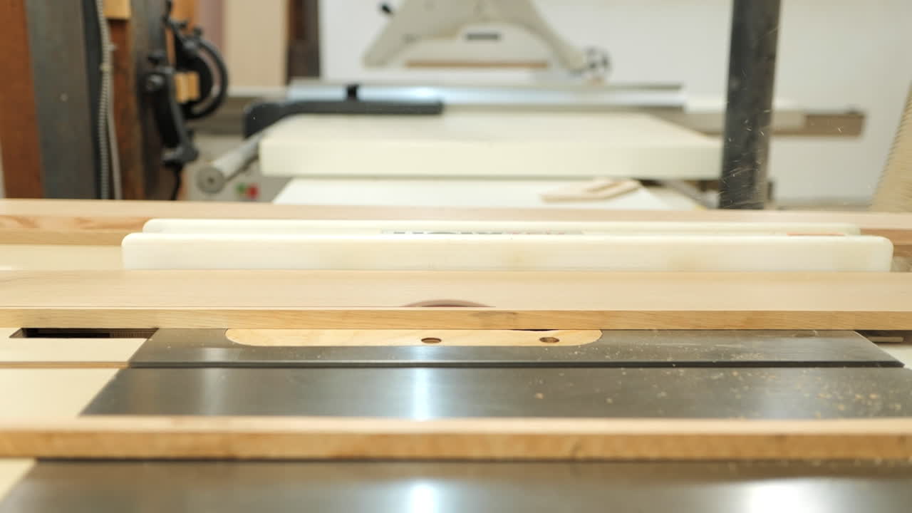 A focused woodworker uses a table saw to shape a piece of wood in a well-equipped workshop. The activity takes place during daylight hours, highlighting craftsmanship and precision.