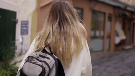 Una-Mujer-Camina-Por-Una-Calle-De-La-Ciudad-Con-Mochila,-Un-Turista-Mira-La-Arquitectura