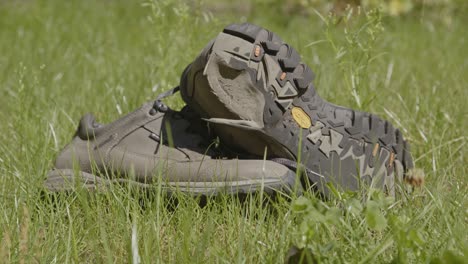 Slow-dolly-out-of-worn-hiking-shoes-lying-in-a-grass-field-on-a-sunny-day