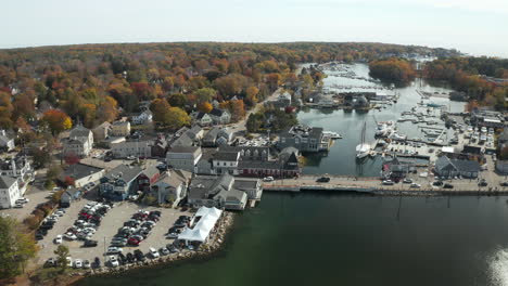 Coastal-town-with-harbor-bordered-by-colorful-woods,-drone-shot