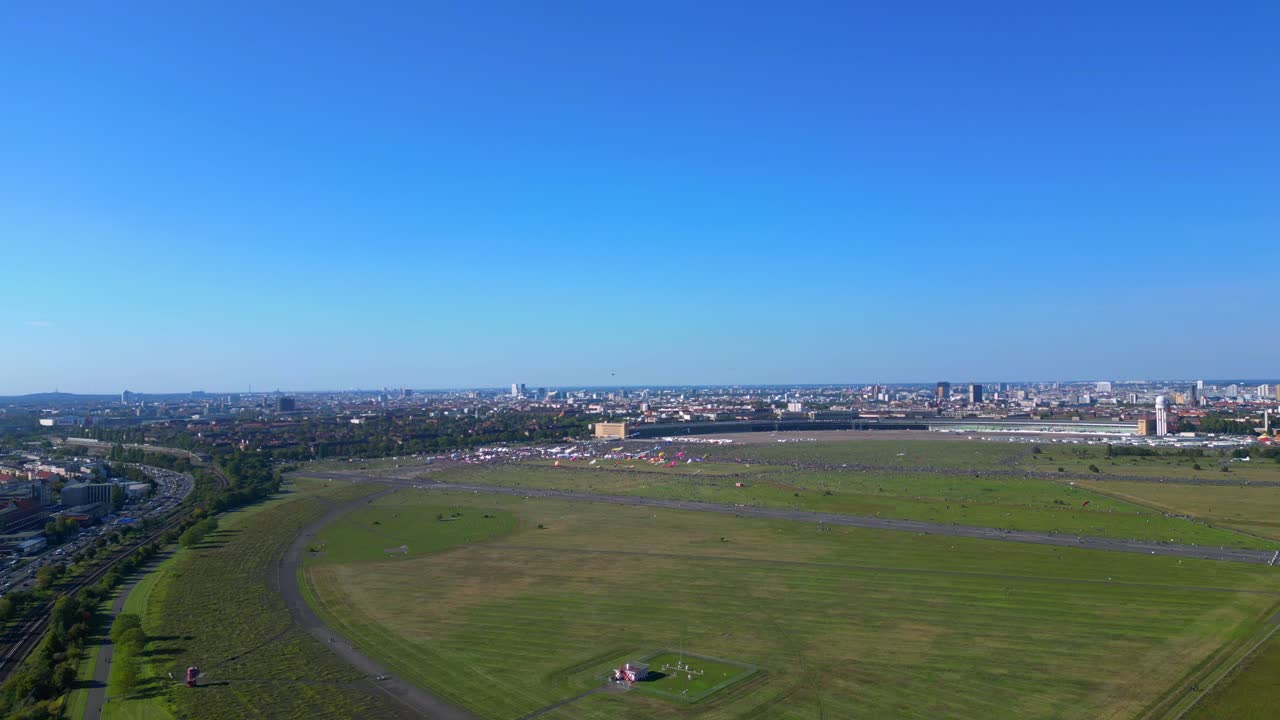 thousands of Berliners enjoying the giant kite festival on a sunny day at Tempelhofer Feld, the former Tempelhof Airport. Lovely aerial view flight descending drone