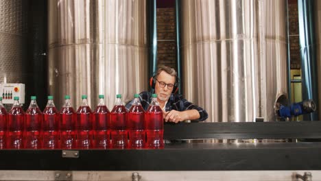 Worker-checking-juice-bottles-on-production-line