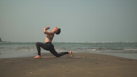 una persona atlética en forma que se dobla hacia atrás mientras se arrodilla durante la práctica de yoga en la playa de arena negra
