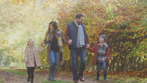 family with mature parents and two children holding hands walking along track in autumn countryside