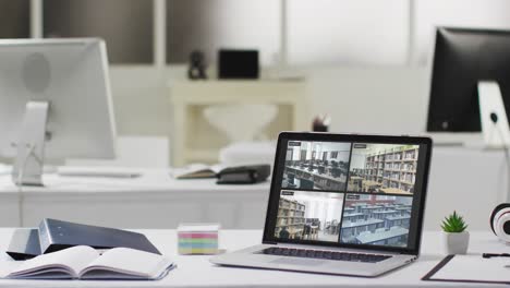 laptop with four security camera views on screen on desk in empty modern office space, slow motion