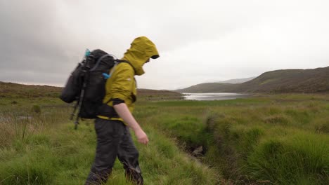 hiking in yellow jacket jumping over stream in scottish landscape