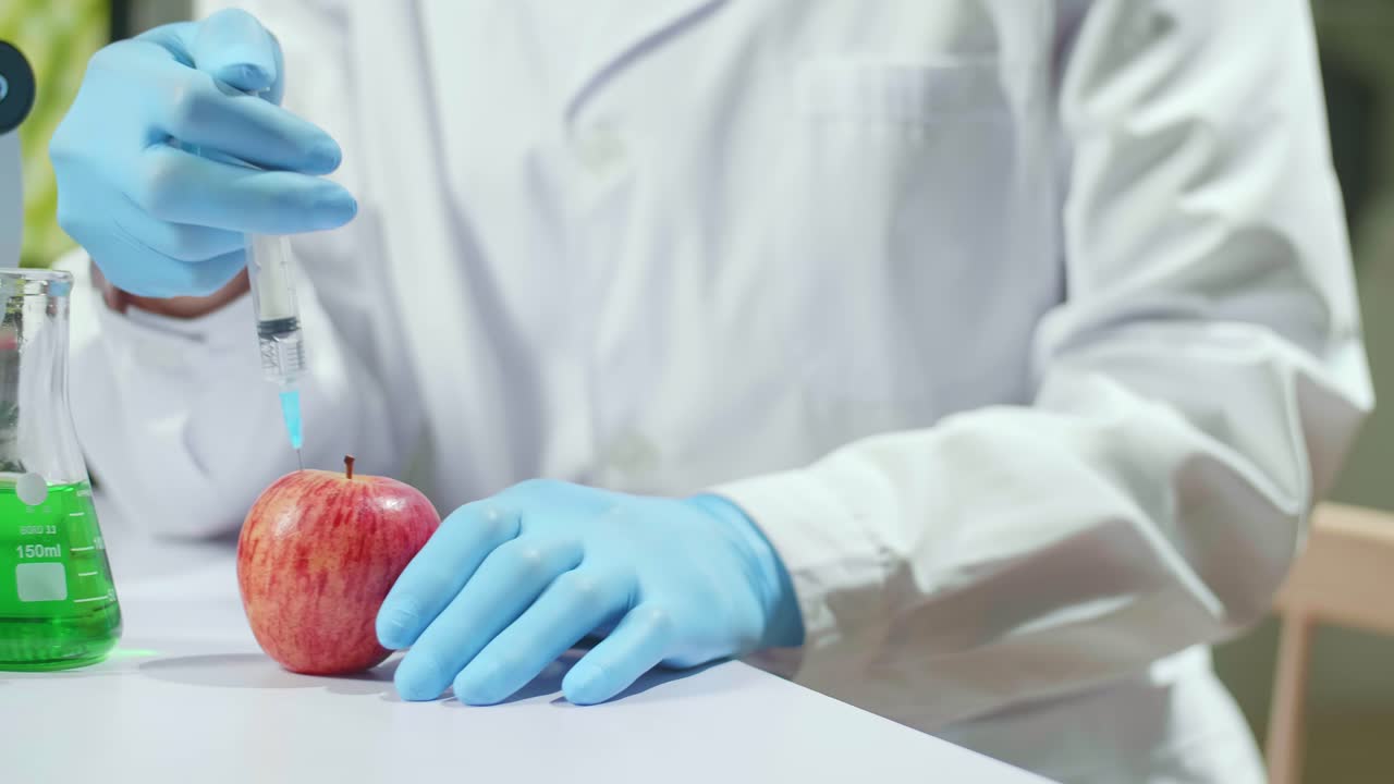 Closeup Of Scientist Injectinging Apple With Genetic Liquid Using Medical Syringe For Microbiology Experiment. Biochemist Working In Pharmaceutical Laboratory Discovery Genetic Mutation Of Vegetables