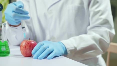 closeup of scientist injectinging apple with genetic liquid using medical syringe for microbiology experiment. biochemist working in pharmaceutical laboratory discovery genetic mutation of vegetables