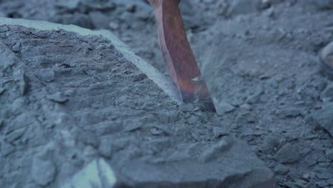 handheld shot of stone craftsman using a handheld pick to edge a large cancagua stone, in the city of ancud on island chiloe