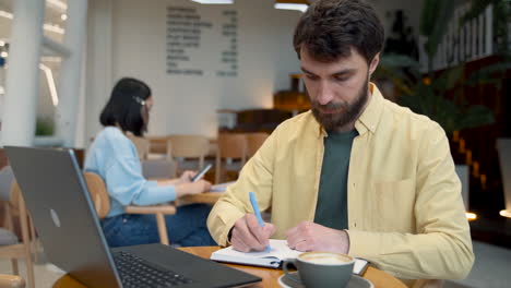 a man takes notes in his notebook in a coffee shop