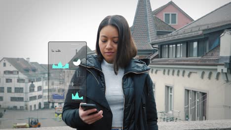 Woman-stands-on-bridge-between-buildings-and-checks-business-data-and-graphs-on-her-smartphone