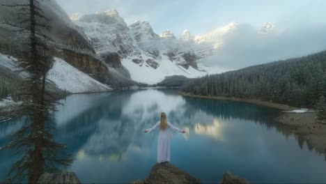 lady in dress slowly raising arms in front of magical reflecting lake and mountains