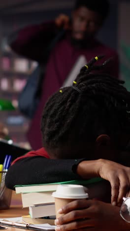 vertical video african american student falling asleep on books pile in the campus library