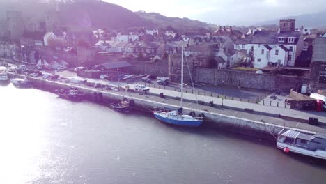 idyllic conwy castle and harbour fishing town boats on coastal waterfront aerial dolly left across shimmering water