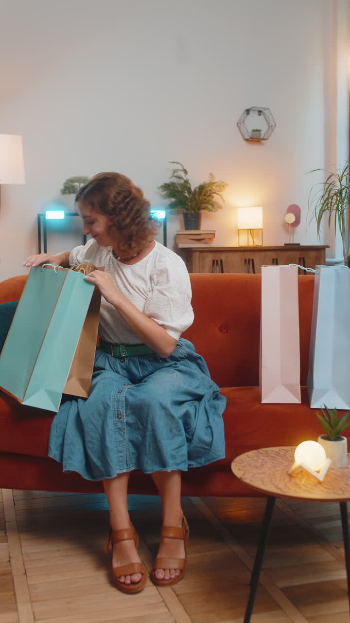 joven feliz caucásica adicta a las compras mujer con bolsas de compras sentada en el sofá en la sala de estar en casa