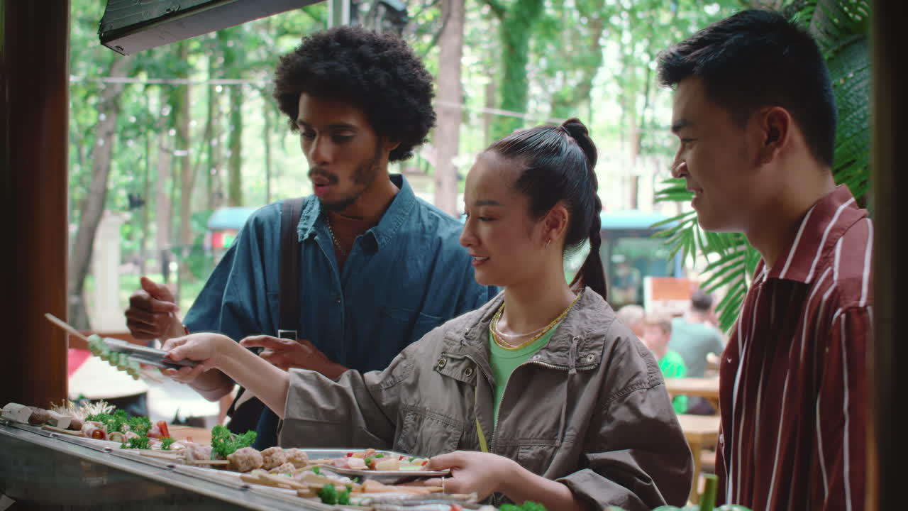 Woman Putting Appetizers on Plate on Street Food Market with Friends