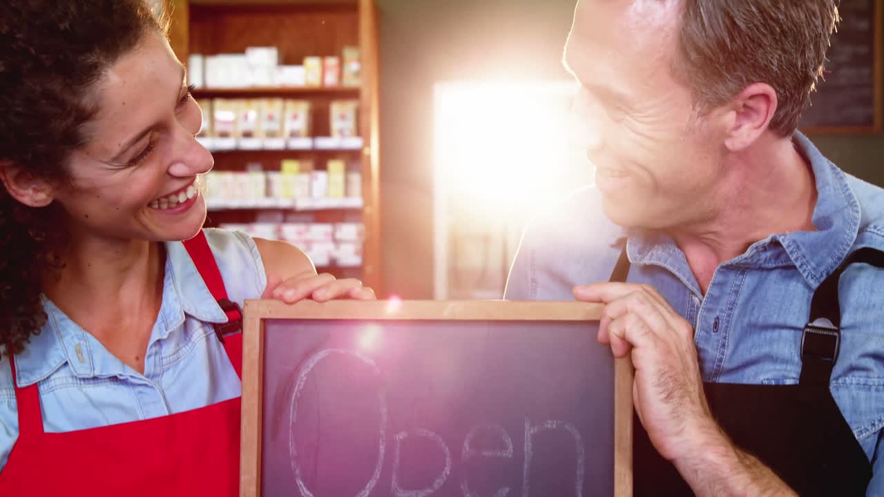 Henkilökunta pitelee avoinna-kylttiä supermarketissa.