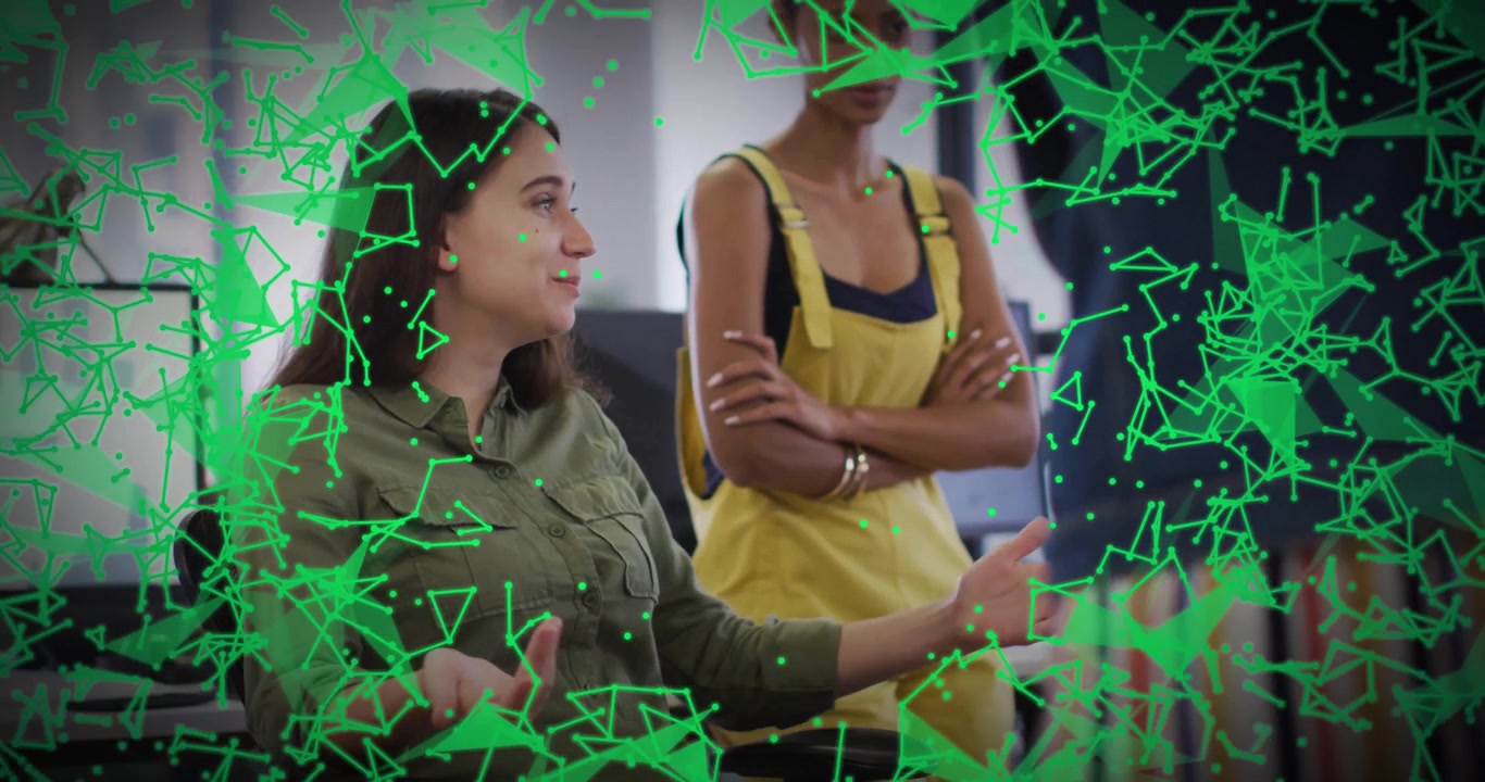 Two female colleagues analyzing network data overlay in tech office, showing floating green nodes