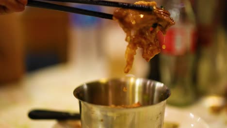 chopsticks lifting braised pork from a pot